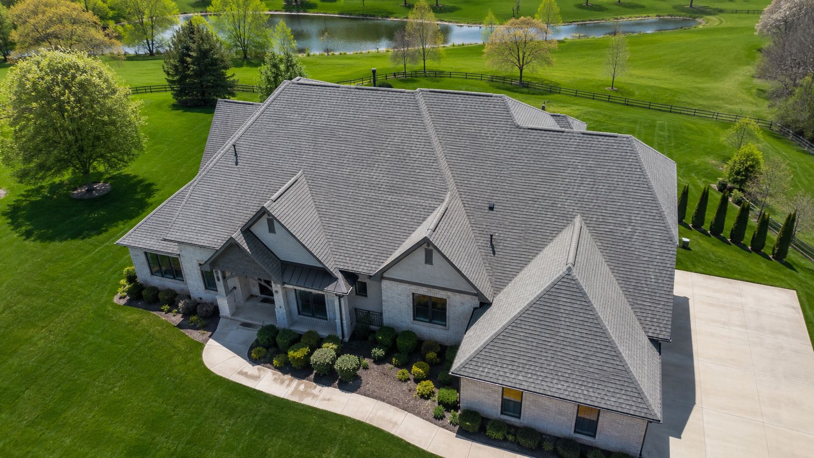 aerial view of a large residential roof surrounded by lawn and a pond